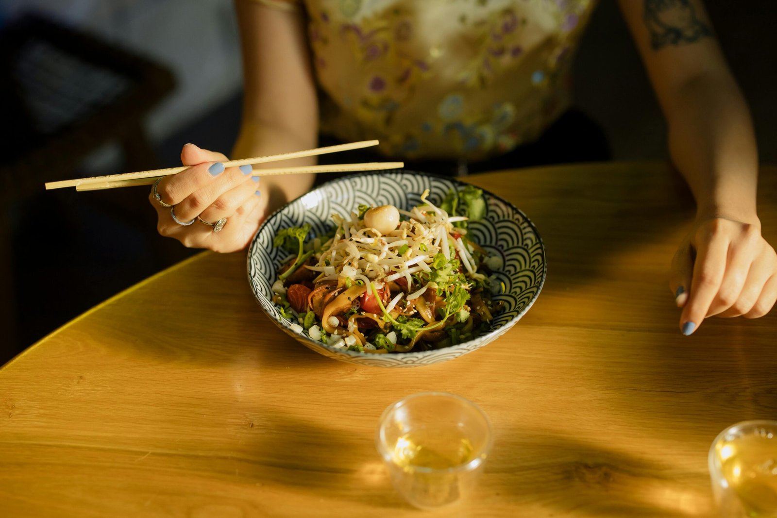Individual savoring Asian fusion salad with chopsticks at a cozy indoor setting.